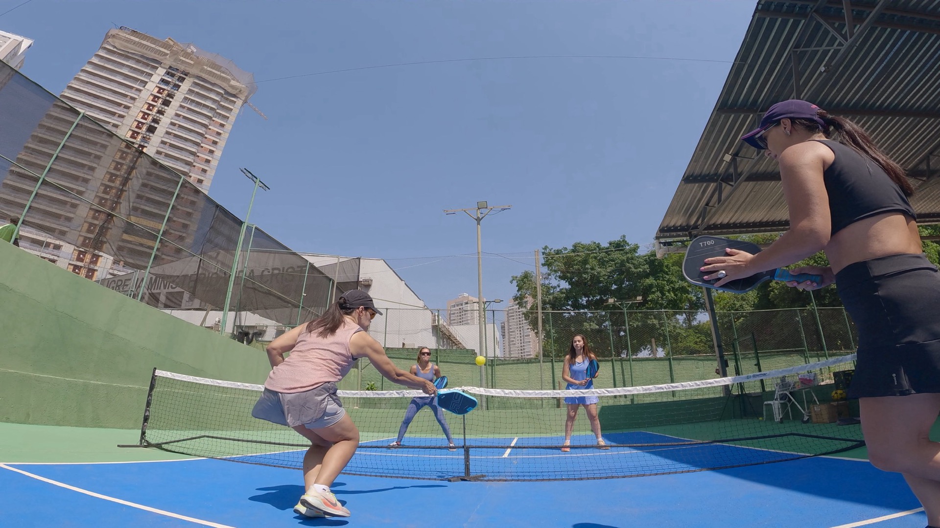 Jogo de pickleball na BTC, quatro jogadoras em ação, prédios ao fundo.